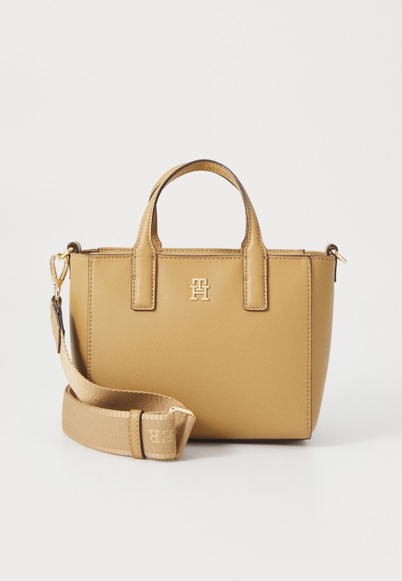 Petit sac à main en cuir marron clair avec doubles poignées, bandoulière large en tissu détachable et emblème logo doré à l'avant.