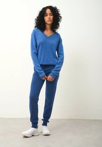 Blå stickad loungewear-set bestående av en långärmad topp med V-ringning och matchande joggerbyxor med dragsko. Mjuk textur, slim fit.