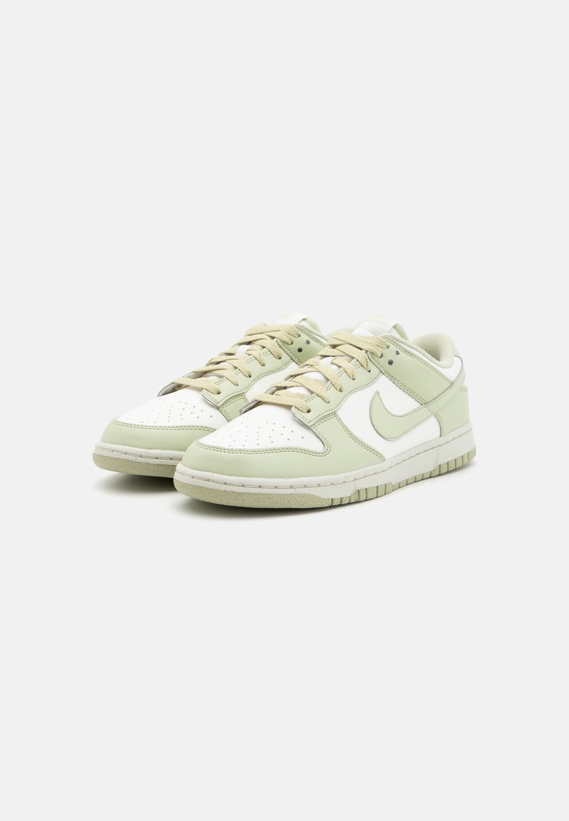 Een paar low-top sneakers met een witte basis en lichtgroene overlays, beige veters en bijpassende lichtgroene Nike Swoosh-logo's.
