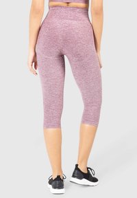 Leggings capri a vita alta in un colore rosa melange con texture, caratterizzati da una vestibilità aderente e seni piatti, abbinati a scarpe da ginnastica nere.