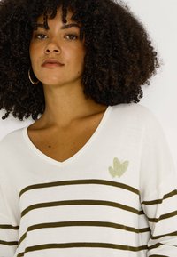 Top de manga larga con rayas blancas y cuello en V, con rayas horizontales verde oliva y un pequeño corazón verde brillante como adorno.