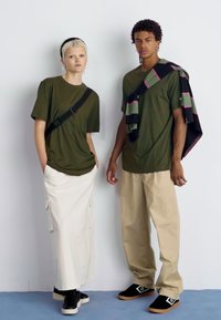 Dwie modelki noszą casualowe ubrania. Po lewej stronie zielona koszulka i biała spódnica; po prawej stronie zielona koszulka z khaki spodniami. Czarne sneakersy i dodatki.