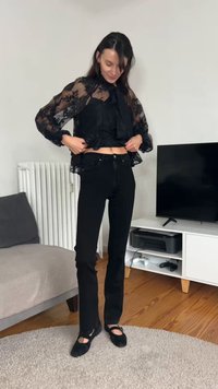 Sort blondebluse med blomsterprint, lagdelt over en sort cropped top. Kombineret med tætsiddende sorte jeans og sorte flade sko. Træ og bløde teksturer i baggrunden.