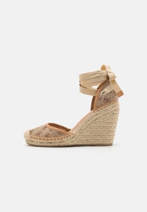 Alpargata de cuña con parte superior de lona beige con un patrón de logotipo, plataforma de yute trenzado y cinta beige para atar al tobillo en forma de lazo.