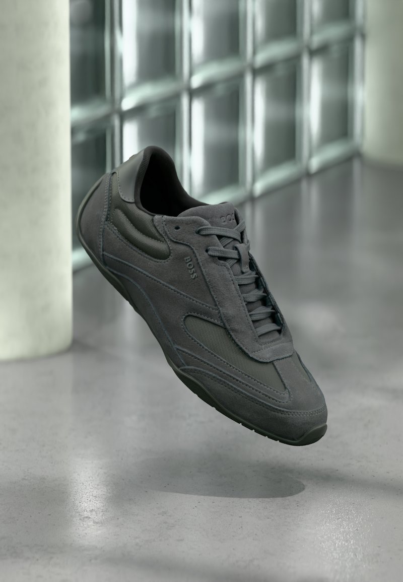 Szare trampki wykonane z połączenia zamszu i siateczki, o niskim kroju, z fakturowanymi detalami, sznurowadłami w tonacji i gumową podeszwą.