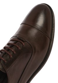 Chaussure en cuir marron à lacets avec une finition lisse et brillante, bout arrondi, couture détaillée et semelle foncée contrastante.