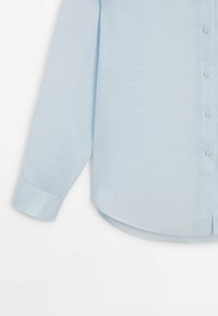 Ljusblå, långärmad skjorta i ett mjukt, strukturerat tyg. Den har en knäppning framtill och en rundad fåll.