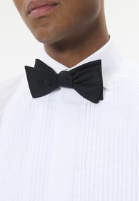 Must mustriba must mahtise pinnaga, kantud valge volditud teksapluusiga. Vibu on sümmeetriline ja hästi määritud servadega.