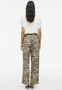 Un pantalon ample à taille haute dans un motif rayé tigre beige et noir, fabriqué à partir d'un tissu lisse. Associé à un t-shirt blanc simple.