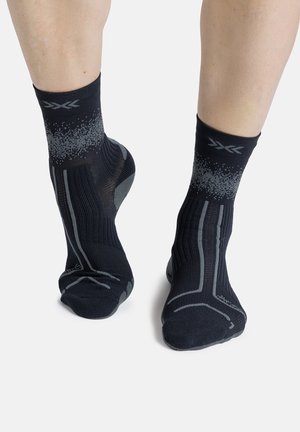 Voeten met zwarte kousen met grijze geometrische patronen en een ademende gebreide textuur tegen een effen lichte achtergrond.