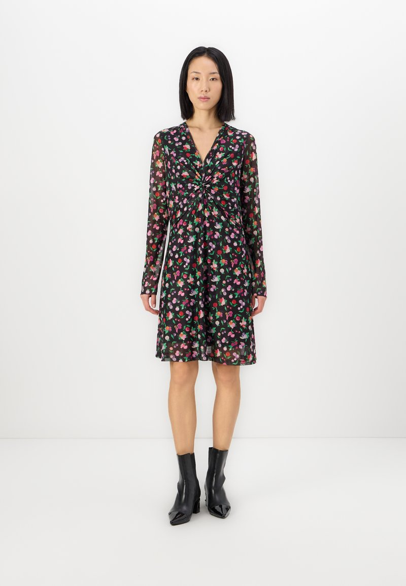 Rochie neagră cu motive florale, cu mâneci lungi, are un detaliu cu nod în față, un model floral multicolor și o tivire evazată, purtată cu botine negre.