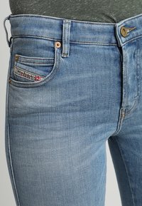 Světle modré džíny z denimu s klasickým pětikapsovým designem, mosazným knoflíkem a jemnou vybledlou texturou. Značka viditelná na kapse.