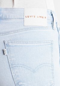 Jeans de mezclilla azul claro con un bolsillo trasero, que presentan una etiqueta blanca con "LEVI'S LINE 8" en impresión metálica y detalles de costura en contraste.
