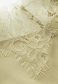 Tissu beige avec superposition de dentelle florale complexe présentant des motifs en maille et des bords délicats à franges.