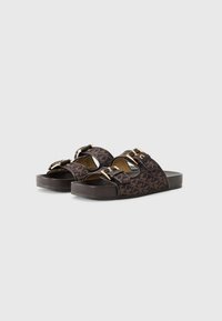 Chanclas marrones con detalles dorados, que presentan una parte superior de tela estampada y una suela de goma gruesa. Decoradas con correas ajustables.
