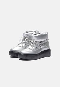 Botas metálicas plateadas hasta el tobillo con un upper acolchado, que presentan cordones grises y una gruesa suela negra de plataforma con estrías verticales.