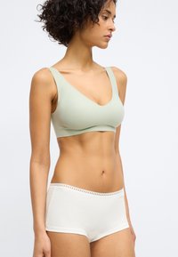 Lys grøn, sømløs bralette med V-hals-design; kombinert med hvite boyshorts med blonderkant rundt livet. Glatt tekstur.