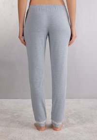 Lichtgrijze pyjamabroek met een elastische tailleband en delicate kantafwerking bij de enkels. Zacht materiaal met een gladde textuur.