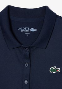Polo shirt marine à coupe ajustée, avec un col côtelé, trois boutons et un logo crocodile Lacoste vert et rouge sur la poitrine gauche.