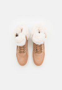 Zapatillas altas de ante en color marrón con un suave cuello de piel sintética blanca, acentos de hardware dorado y cordones dorados. Diseño texturizado y acolchado.