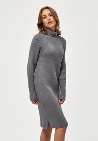 Grå ribbad stickad klänning med hög krage och långa ärmar, med sidokanter vid fållen för ökad rörelse och textur.