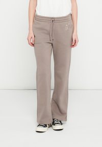 Szare dresowe spodnie z szerokimi nogawkami, elastycznym pasem, bocznymi kieszeniami oraz naszytym logo „GAP” na biodrze, zestawione z czarnymi trampkami.