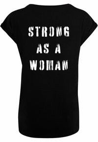 Sort T-shirt med korte ærmer, der har teksten "STÆRK SOM EN KVINDE" i hvid, fed, slidt skrifttype på ryggen. Glat bomuldsstruktur.