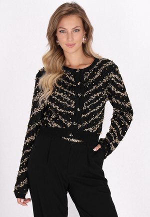 Zwarte gebreide cardigan met een gouden zigzagpatroon en decoratieve kralen, met hartvormige knopen en een getailleerde taille.