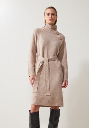 Strickkleid in Beige mit hohem Kragen, Seitenknöpfen und tailliertem Gurt. Mit gerippten Bündchen und Saum. Glatte, weiche Textur.