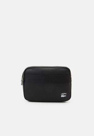 Trousse rectangulaire noire Lacoste avec poche avant zippée et tirette argentée, arborant le logo blanc Lacoste avec motif crocodile.