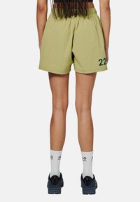 Olivgrüne Shorts mit einem elastischen Taillenbund und einer großen "22" in Dunkelgrün bedruckt. Getragen mit weißen Socken und schwarzen Sneakern.