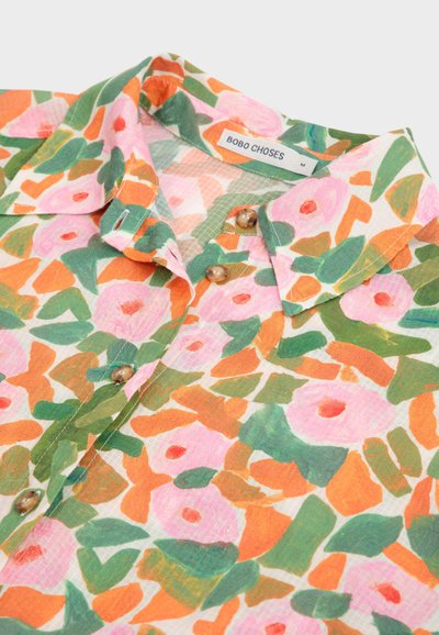 Camicia floreale multicolore con colletto, bottoni e un tessuto morbido e texture, caratterizzata da un vivace pattern arancione, rosa e verde.