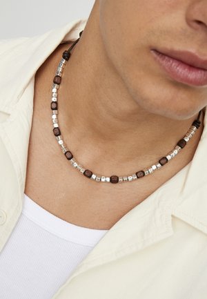 Collar de cuentas que presenta cuentas de madera y metálicas en tonos marrón y plateado, con un acabado texturizado, asegurado con un cordón marrón.