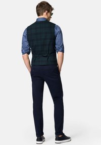 Zielono-granatowa kamizelka w kratę nałożona na jasnoniebieską koszulę, w połączeniu z ciemnoniebieskimi spodniami i czarnymi sneakersami, widok z tyłu.