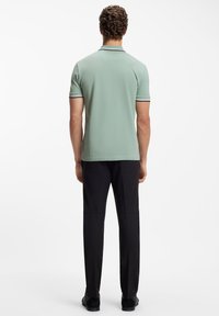 Polo-shirt i lysegrøn, struktureret stof med sorte og hvide stribede detaljer på kraven og ærmerne. Sammen med sorte bukser.