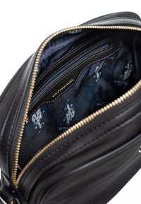 Interno di una borsa in pelle nera con tasche con zip e foderato in tessuto stampato con logo. Dettagli della cerniera dorati e superficie texture visibili.