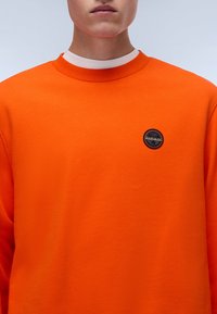 Felpa arancione in misto cotone, con collo tondo, polsini a coste e una piccola etichetta nera con logo sul petto.