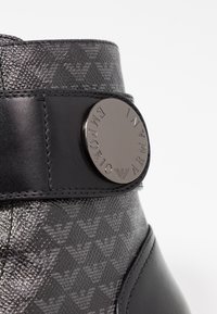Černé kotníkové boty s texturovaným vzorem a lesklým kovovým logem. Hladká kožená látka a kontrastní vzorovaná horní část.