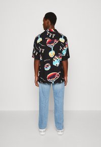 Camicia nera a maniche corte con una stampa vivace di bicchieri da cocktail e dadi, vestibilità rilassata, tessuto leggero e orlo arrotondato.