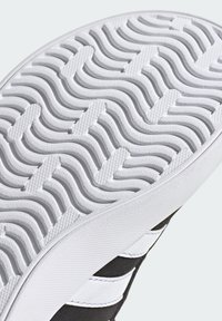 Schoenzool met een golvende textuur in wit rubber en geprofileerde gleuven voor grip. Zwart bovenwerk met witte strepen en accenten.