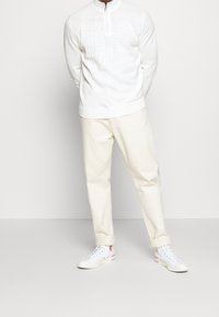 Weißer Strick-Half-Zip-Pullover, cremefarbene Chinos und weiße Sneaker mit roten Akzenten. Der Pullover hat gerippte Bündchen und einen Saum für zusätzliche Textur.