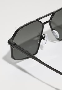 Occhiali da sole rettangolari neri con lenti grigie, montatura in metallo e logo "Michael Kors" inciso sulle astine. Inclusi naselli regolabili.