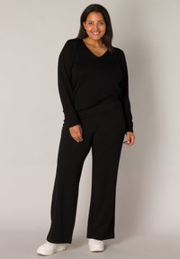 Zwart bijpassend set bestaande uit een top met lange mouwen en een V-hals en brede broek, beide in een zachte textuur. Gekocht met witte sneakers.