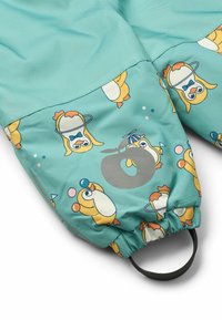 Türkiser Stoff mit einem durchgehenden Pinguin-Muster. Elastischer Saum mit einer schwarzen Schlaufe zum Befestigen. Glatte Textur und verspieltes Design.