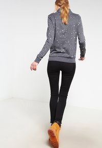 Sweat-shirt gris avec un imprimé discret d'oiseaux, associé à un jean noir ajusté et des bottines marron clair. Le tissu semble doux avec des poignets côtelés.