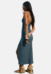 Ribbed maxi dress in dark blue with back tie straps, side slit, and ornamental chain accent. Paired with tan ankle boots.
