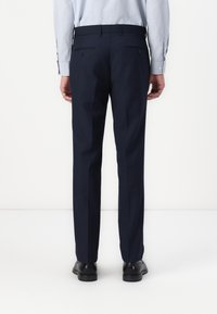 Navy tailored trousers with a straight leg design, two back pockets, and a smooth texture. Paired with black shoes.