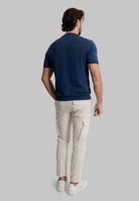Maglietta a maniche corte navy in maglia, abbinata a pantaloni cargo beige con tasche laterali e sneakers bianche. Design semplice e funzionale.