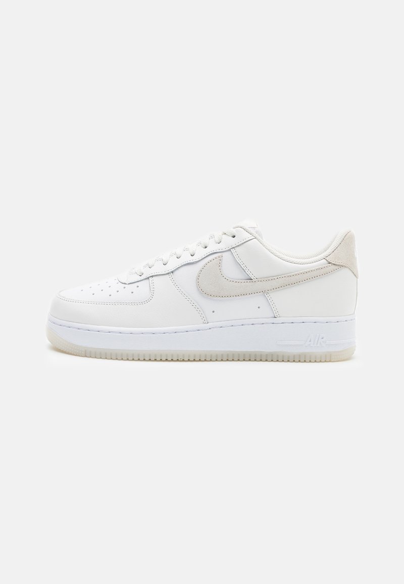 White leather sneaker with a smooth finish, round toe, lace-up front, and contrasting beige suede swoosh. Textured rubber sole with "AIR" branding.