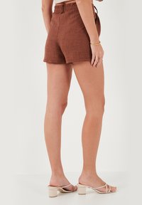 Shorts en lin marron avec une texture; taille élastique, poches avant plates et coupe décontractée. Assortis avec des sandales à talons bloc de couleur claire.